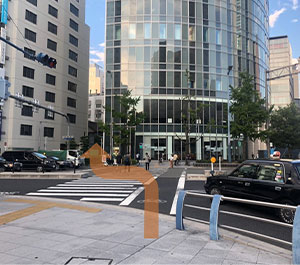 When you reach the top of the stairs, you will see a crosswalk. Cross it and go to the left of the building with glass windows.